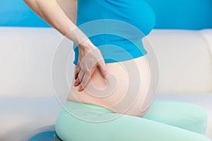 Pregnant woman sitting on fit ball holds hand on her back