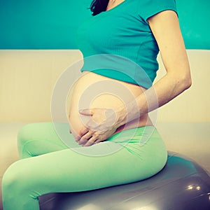 Pregnant woman sitting on fit ball, touching her belly