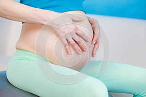 Pregnant woman sitting on fit ball, touching her belly
