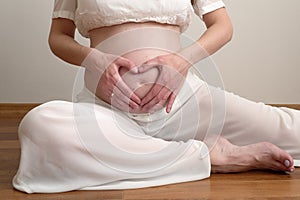 pregnant woman sitting on floor in kapotasana pose and make heart shaped hand show love. health care pregnacy concept.