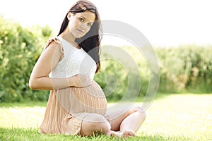 Pregnant Woman Sitting On Grass Outdoors Holding Bump