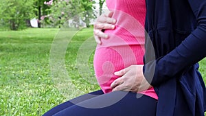 Pregnant woman sitting on grass and stroking her stomach