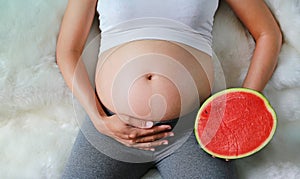 Pregnant woman sitting and holding cut half watermelon at her belly