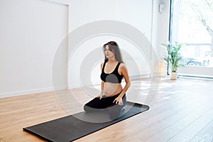 Pregnant woman sitting on a mat, practicing yoga alone in a big studio