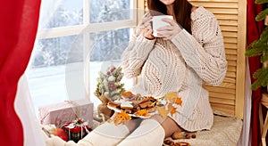 Pregnant woman sitting near the window, beautiful winter landscape with snowy forest is outside the window, christmas decoration