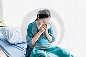 Pregnant woman Sitting in the patient`s bed in the hospital, using a paper towel to wipe the snot Because of the flu and Virus in