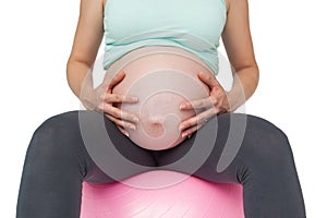 Pregnant woman sitting on pink exercise ball holding her bump