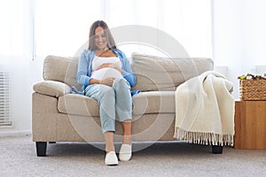 Pregnant woman sitting on sofa in casual comfortable clothes