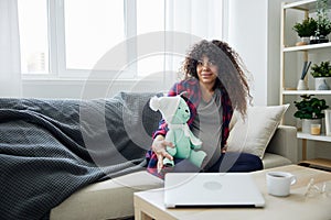 A pregnant woman sitting on the sofa with children& x27;s toy rabbit in her hands Easter, talking to the child, smiling