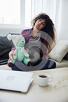 A pregnant woman sitting on the sofa with children& x27;s toy rabbit in her hands Easter, talking to the child, smiling