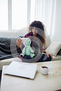 A pregnant woman sitting on the sofa with children& x27;s toy rabbit in her hands Easter, talking to the child, smiling