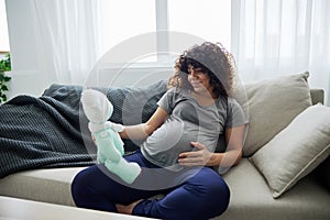 A pregnant woman sitting on the sofa with children& x27;s toy rabbit in her hands Easter, talking to the child, smiling