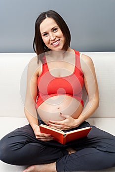 Pregnant woman sitting on sofa and holding book