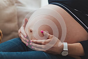 Pregnant woman sitting on sofa and holding her belly close up