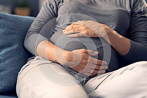Pregnant woman sitting on the sofa and holding her belly