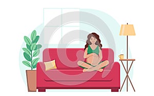 A pregnant woman is sitting on the sofa , smiling and hugging her big belly.