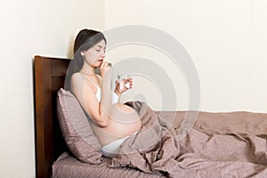 Pregnant woman is sitting in sofa. Taking pills from colds. Last months of pregnancy