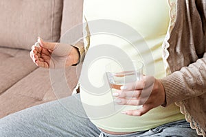 Pregnant woman is sitting in sofa. Taking pills from colds. Last months of pregnancy