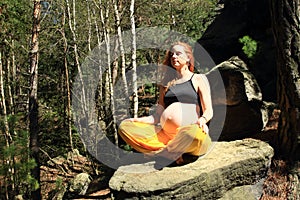 Pregnant woman sitting on stone in easy yoga pose