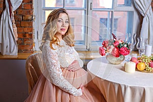 Pregnant woman sitting at the table in a beautiful dress, the concept of motherhood