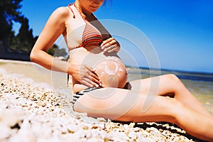 Pregnant woman skin care moisturizer cream on belly on beach at