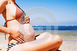 Pregnant woman skin care moisturizer cream on belly on beach at