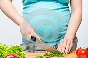 Pregnant woman slices fresh herbs on a cutting board