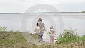 Pregnant woman and small girls are on the beach of a forest lake.