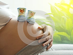 Pregnant woman with small shoes for the unborn baby on the belly.