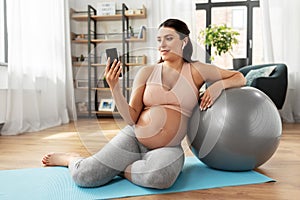 Pregnant woman with smartphone and fitball at home