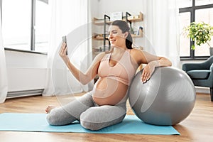 Pregnant woman with smartphone and fitball at home