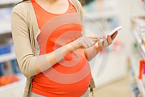 Pregnant woman with smartphone at pharmacy