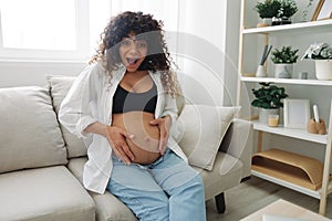 Pregnant woman smile and happiness sits on the couch freedom and strokes her belly feels kicks with the baby in the