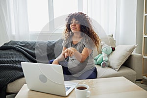 Pregnant woman smile sits at home on the couch with a laptop and talks with a doctor on video chat, freelancer works