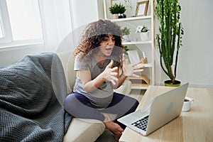 Pregnant woman smile sits at home on the couch with a laptop and talks with a doctor on video chat, freelancer works