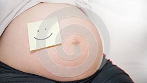 Pregnant woman with smile yellow post-it on her belly