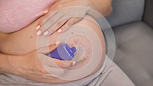 A pregnant woman smokes a vape while sitting on the couch. Close-up of the belly with allergies.