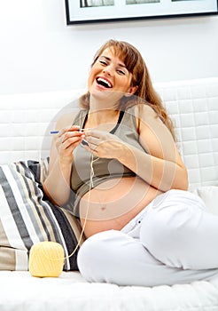 Pregnant woman on sofa knitting for her baby