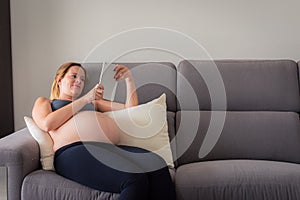 Pregnant Woman On Sofa Relaxing With Digital tablet reading some pregnancy tips