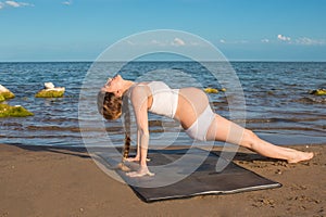 Pregnant woman in sports bra doing exercise on yoga pose on sea