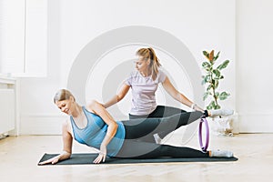 Pregnant woman in sports uniforms with coach doing gymnastic in the bright studio