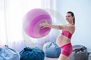 A pregnant woman in sportswear is doing gymnastics for pregnant women. The girl is engaged in fitness with a ball for