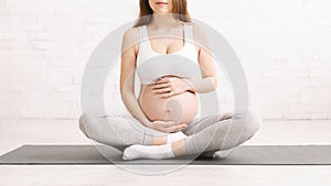 Pregnant woman in sportswear sitting on yoga mat