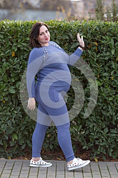 Pregnant woman in sportswear walks along clipped shrubbery photo