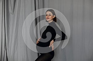 Pregnant woman standing against gray background wearing black clothes