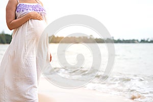 Pregnant woman standing on beach hand touching on her belly.