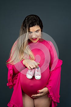 Pregnant woman standing holding baby shoes over her belly