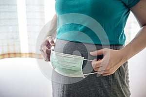 Pregnant woman standing and holding a hygienic face mask with 2 hands. Place at belly