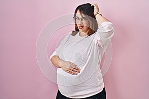 Pregnant woman standing over pink background confuse and wondering about question