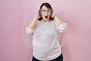 Pregnant woman standing over pink background crazy and scared with hands on head, afraid and surprised of shock with open mouth